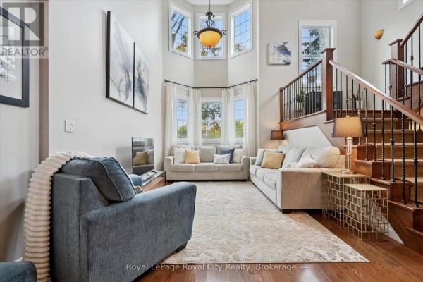 Living room with gray sofas, blue armchair, ottoman, television, and a bay window overlooking trees. - 6 - 12 Glasgow Street S, Guelph