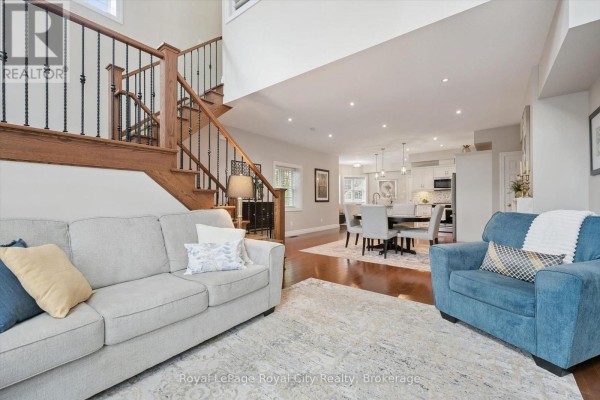 Living room and dining area with sofas, armchair, dining table, chairs, and a wooden staircase. - 6 - 12 Glasgow Street S, Guelph