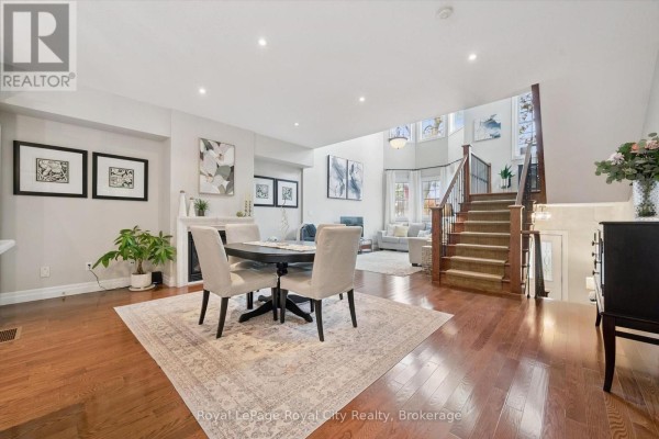 Dining area with a round table, chairs, fireplace, and view of the living room and staircase. - 6 - 12 Glasgow Street S, Guelph