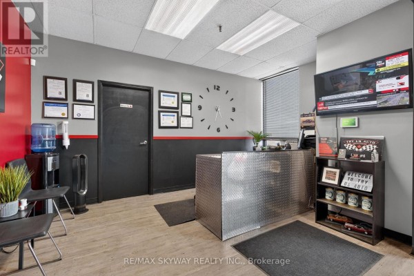 Reception desk and waiting area inside an auto repair shop with a large clock. - 6 - 181 Rutherford Road, Brampton