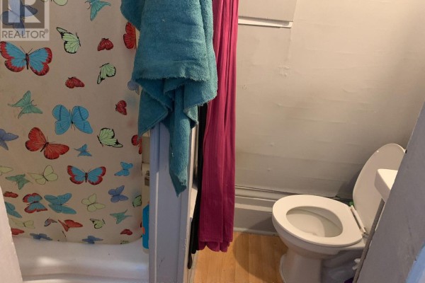Small bathroom with a toilet, bathtub with butterfly shower curtain, and wooden floor. - 6 - 2 Bascom Street S, Uxbridge