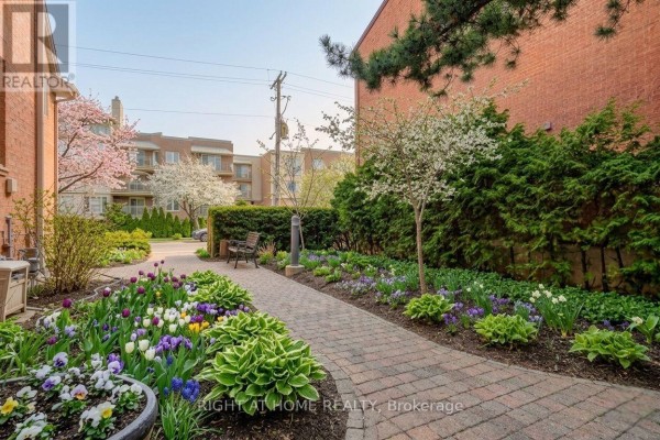 Townhouse exterior featuring blooming trees and balconies, with a clear blue sky. - 6 - 2 Columbus Avenue, Ottawa