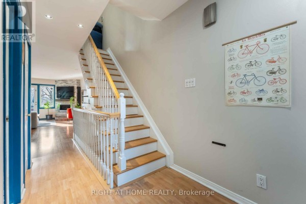 Interior view of entryway with staircase, wooden floors, and wall-mounted bicycle art. - 6 - 2 Columbus Avenue, Ottawa