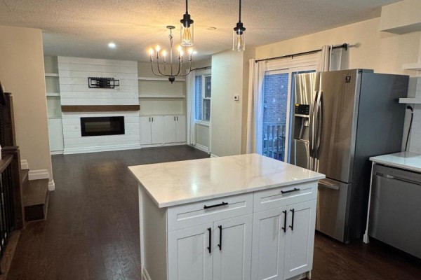 Interior view of a modern kitchen with white cabinetry, stainless steel appliances, and a large island. - 6 - 230 Clarke Road, London East