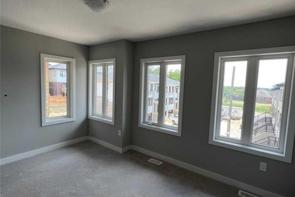 Bedroom with light grey walls, beige carpet, and three windows. - 6 - 527 Shaver Road, Hamilton