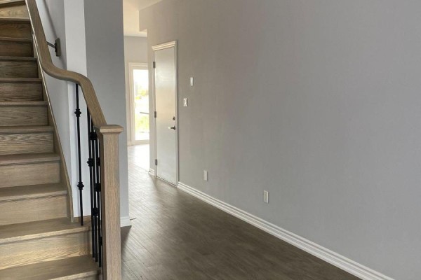 Hallway with wood-look flooring, grey walls, a closed white door, and the start of a wooden staircase. - 6 - 5672 Dorchester Road, Niagara Falls