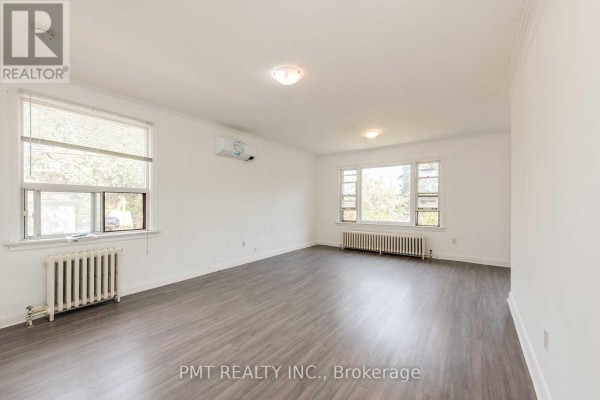 Living room with white walls, grey wood-look flooring, white radiator, and large windows with blinds. - 6 - 58 Leyton Avenue, Toronto
