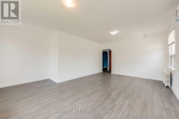 Empty living room with white walls, grey wood-look flooring, radiator, and an archway leading to another room. - 6 - 58 Leyton Avenue, Toronto