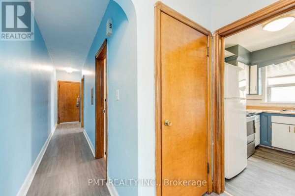 Hallway with light blue walls, grey wood-look flooring, and wooden doors. Kitchen visible to the right. - 6 - 58 Leyton Avenue, Toronto