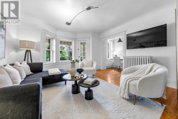 Living room with bay windows, black sectional sofa, white chairs, and a large rug. - 6 - 68 Kendal Avenue, Toronto