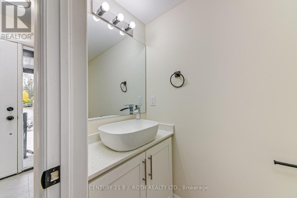 Powder room with white vanity, vessel sink, chrome faucet, large mirror, and overhead lighting. - 6 - 98 Peel Street, Barrie