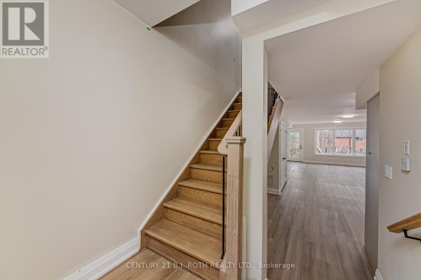 Interior hallway with wood staircase leading up and view of an open living area with large windows. - 6 - 98 Peel Street, Barrie