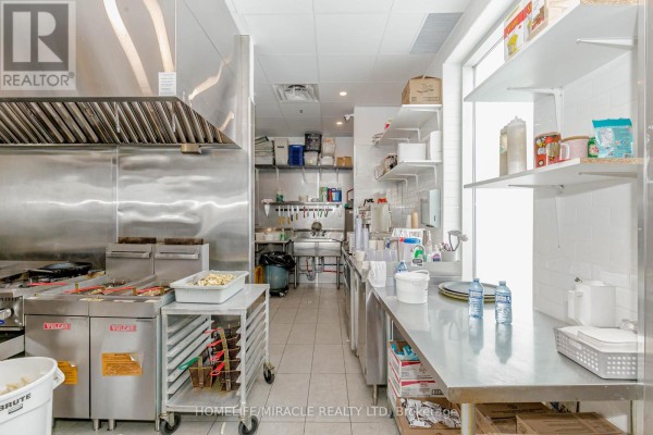 Commercial kitchen with stainless steel counters, shelves stocked with supplies, and tiled walls. - 6 & 7 - 1840 Major Mackenzie Drive, Vaughan