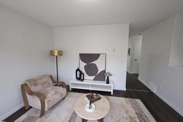 Living room with armchair, white media console with artwork, and dark wood floors. - #6 16777 91 St Nw Nw, Edmonton
