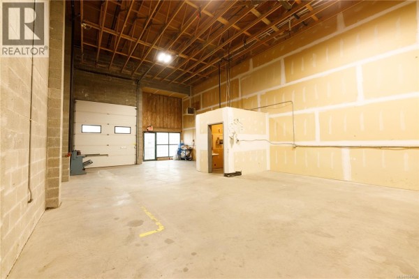 Warehouse area with wooden panels and concrete flooring, showing ample space. - 6 2535 Mccullough Rd, Nanaimo