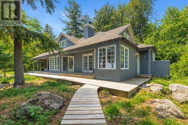 Gray house with wrap-around wooden deck and large windows, surrounded by trees. - 6 29c Mowat Island, Carling