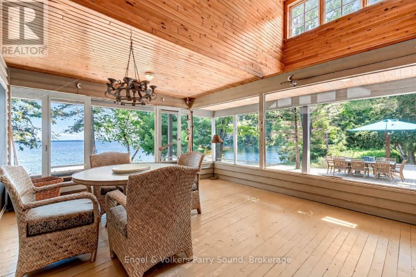 Sunroom with wicker chairs, dining table, sofa, and large windows with lake views. - 6 29c Mowat Island, Carling