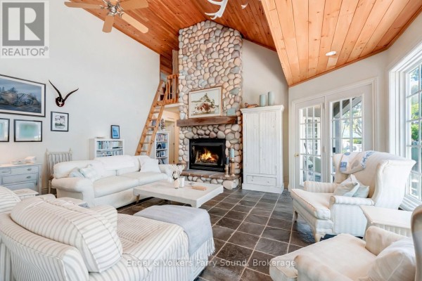Living room with stone fireplace, white sofas, and wooden vaulted ceiling with loft access. - 6 29c Mowat Island, Carling