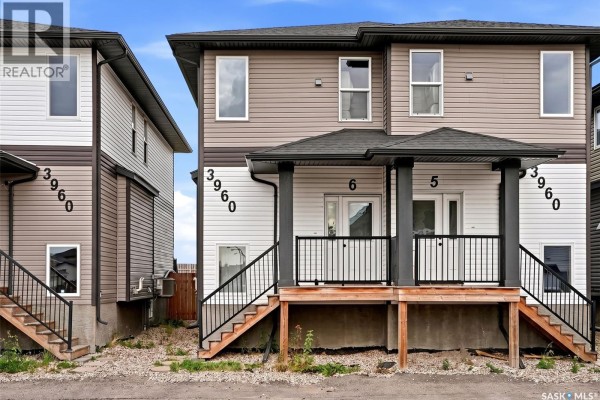 Front entrance of a duplex with a covered porch, stairs, and dark railings. - 6 3960 7th Avenue E, Regina
