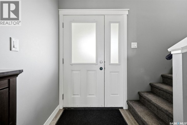Interior view of a front door with frosted glass panels and a black doormat on wood-look flooring. - 6 3960 7th Avenue E, Regina