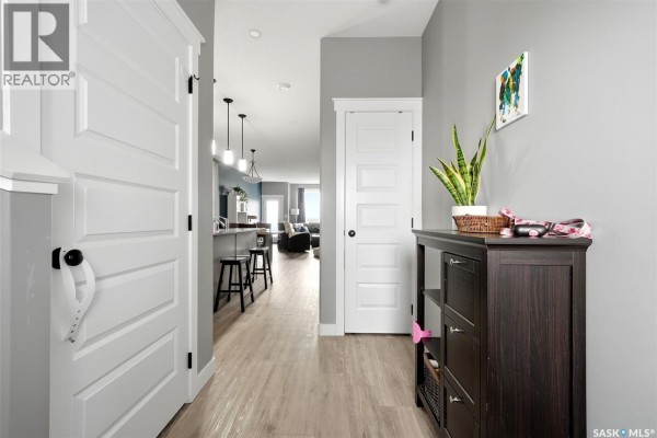 Hallway view with light wood-look flooring, grey walls, white doors, and a dark wood console table. - 6 3960 7th Avenue E, Regina