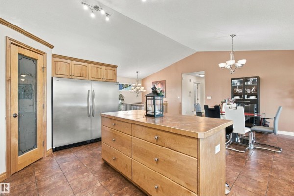 Kitchen island and stainless steel refrigerator with a dining area visible in the background. - #6 61130 Rr 465, Rural Bonnyville M D 