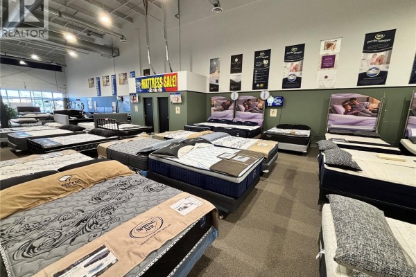 Mattress store interior with numerous beds on display, varied styles and brands, under fluorescent lighting. - 6 805 Circle Drive E, Saskatoon