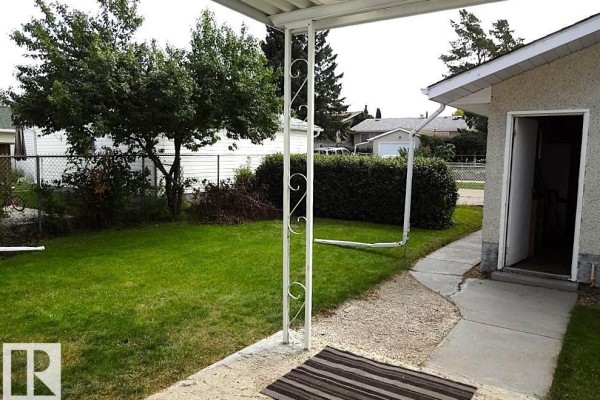 View from under a covered patio looking towards a grassy backyard and a detached garage. - 6 Beverly Av, Spruce Grove