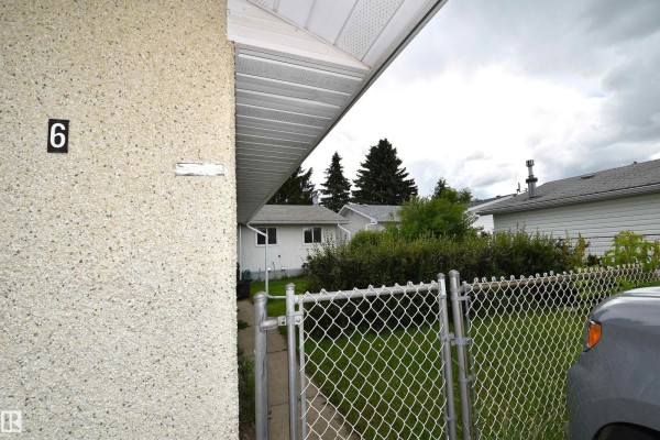 View of the house number 6 on a textured wall, with a chain-link gate and driveway. - 6 Beverly Av, Spruce Grove