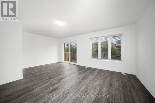 Living room with a large window, sliding glass door to a wooden deck, and dark wood flooring. - 6 Blue Forest Crescent, Barrie
