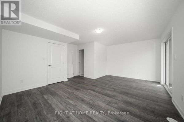 Finished basement room with white walls, dark wood flooring, and a sliding glass door on the right. - 6 Blue Forest Crescent, Barrie