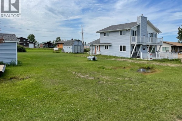 Wide angle view of the light blue house and its grassy yard with several small storage sheds on the property. - 6 Bronco Drive, Delaronde Lake