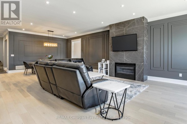 Living room with grey paneled walls, a grey marble fireplace with a television, and a black leather recliner. - 6 Caldwell Drive, Oro Medonte