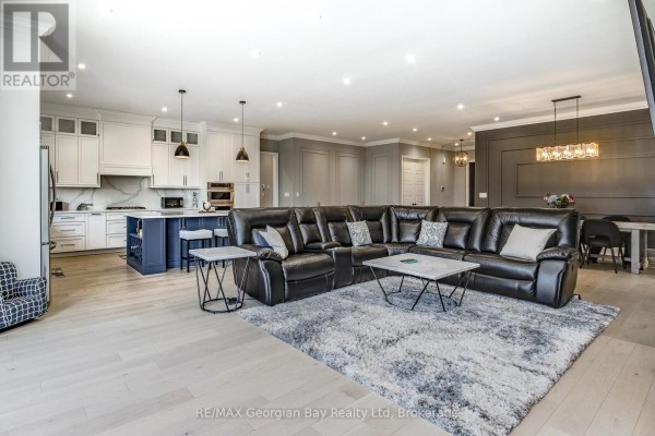 Open concept living area with a large sectional sofa, kitchen with white cabinets and a blue island, and dining area. - 6 Caldwell Drive, Oro Medonte