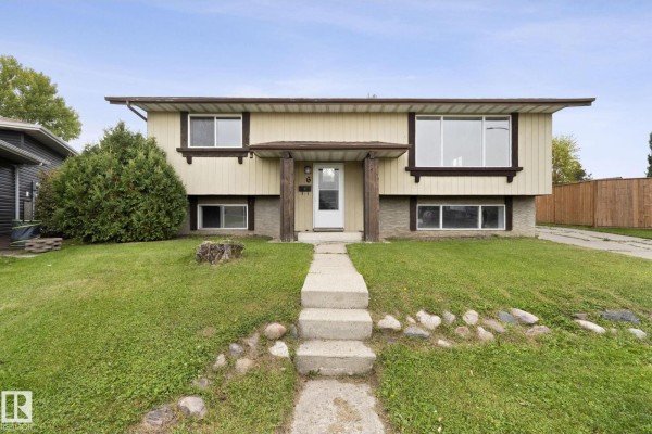 Front exterior of a split-level home with beige siding, stone accents, and a concrete pathway. - 6 Campbell Cres E, Stony Plain