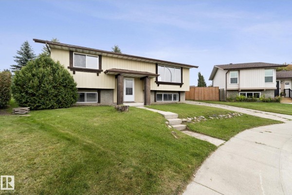 Side view of a split-level home with beige siding, green lawn, and neighboring houses. - 6 Campbell Cres E, Stony Plain