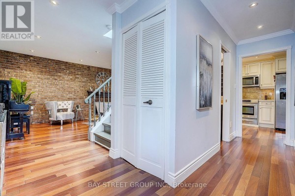 Interior hallway with hardwood floors, white bi-fold doors, and a view of the kitchen and living area. - 6 Caravan Drive, Toronto