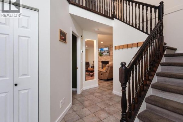 Interior view of a hallway with tile floor, white doors, a dark wood staircase, and a mirror. - 6 Carnelian Court, Whitehorse