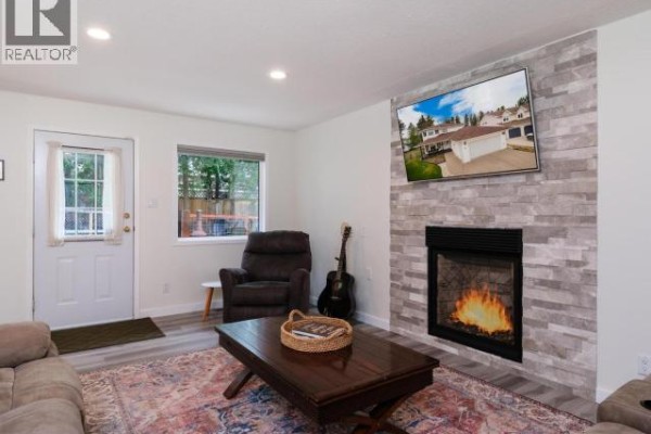 Living room featuring a fireplace with stacked stone surround, television, recliner, coffee table, and a guitar. - 6 Carnelian Court, Whitehorse