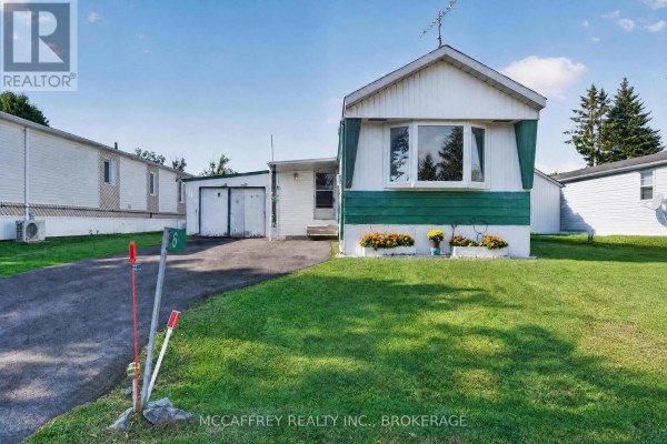 Street view of a mobile home with a dark asphalt driveway and green lawn. - 6 Cedar Street, Greater Napanee