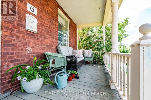 Close-up of the covered porch with wicker furniture, potted plants, a watering can, and white railings. - 6 Crawford Street, Whitewater Region