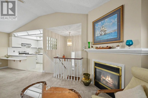 Living room with fireplace, vaulted ceiling, and view of the kitchen and staircase. - 6 Donald Crescent, Wasaga Beach