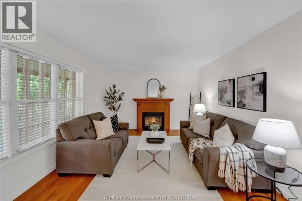 Living room with two brown sofas, a fireplace with a wooden mantel, and hardwood floors. - 6 James Street, Blenheim