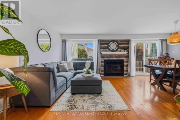 Living room with grey sectional sofa, ottoman, fireplace with stone surround, and dining area with wooden table. - 6 Maravista Drive, Ottawa