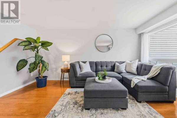 Living room with a grey tufted sectional sofa, ottoman, and a large window with blinds on the right. - 6 Maravista Drive, Ottawa