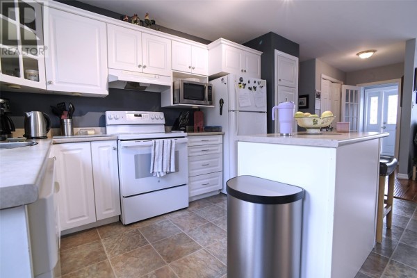 White kitchen cabinets and countertops with white appliances, a microwave, and a kitchen island with bar stools. - 6 Noad Place, St  John S