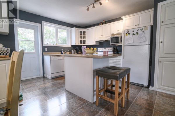 Kitchen with white cabinets, white appliances, a kitchen island with bar stools, and a door leading outside. - 6 Noad Place, St  John S