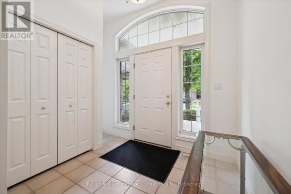 Foyer with double white doors, a large arched window above the entrance, and double cream closets. - 6 Parkside Drive, Guelph