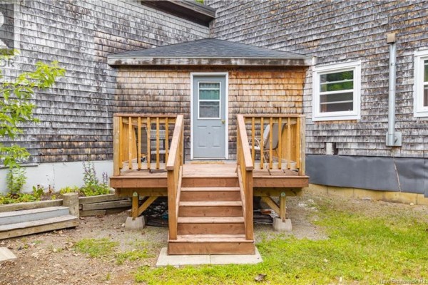 Rear wooden deck with stairs leading to a grey door, surrounded by grass and trees. - 6 Parkwood Drive, St  Stephen