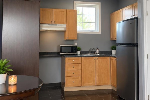 A compact kitchen with light wood cabinets, black countertops, stainless steel refrigerator, and microwave. - 6 Quincy Place N, Brampton